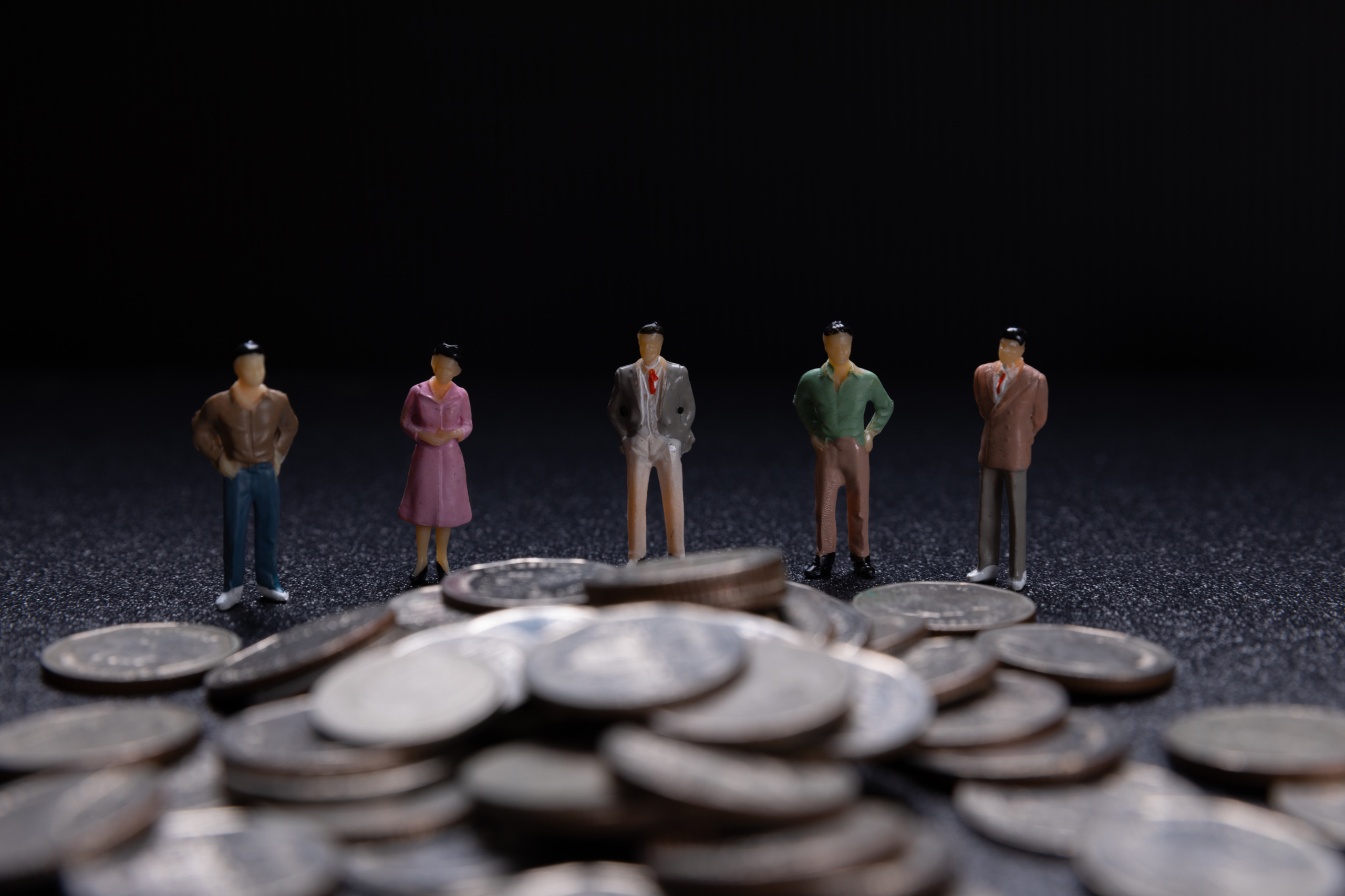 Bonecos de roupa social alinhados em frente a diversas moedas